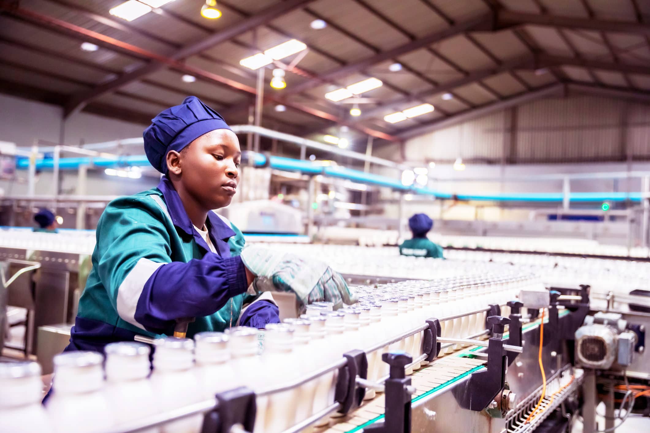 Africa, Industries, Business, Factory - A Female African Factory worker checking the freshly filled milk bottles on the conveyor belt at a factory