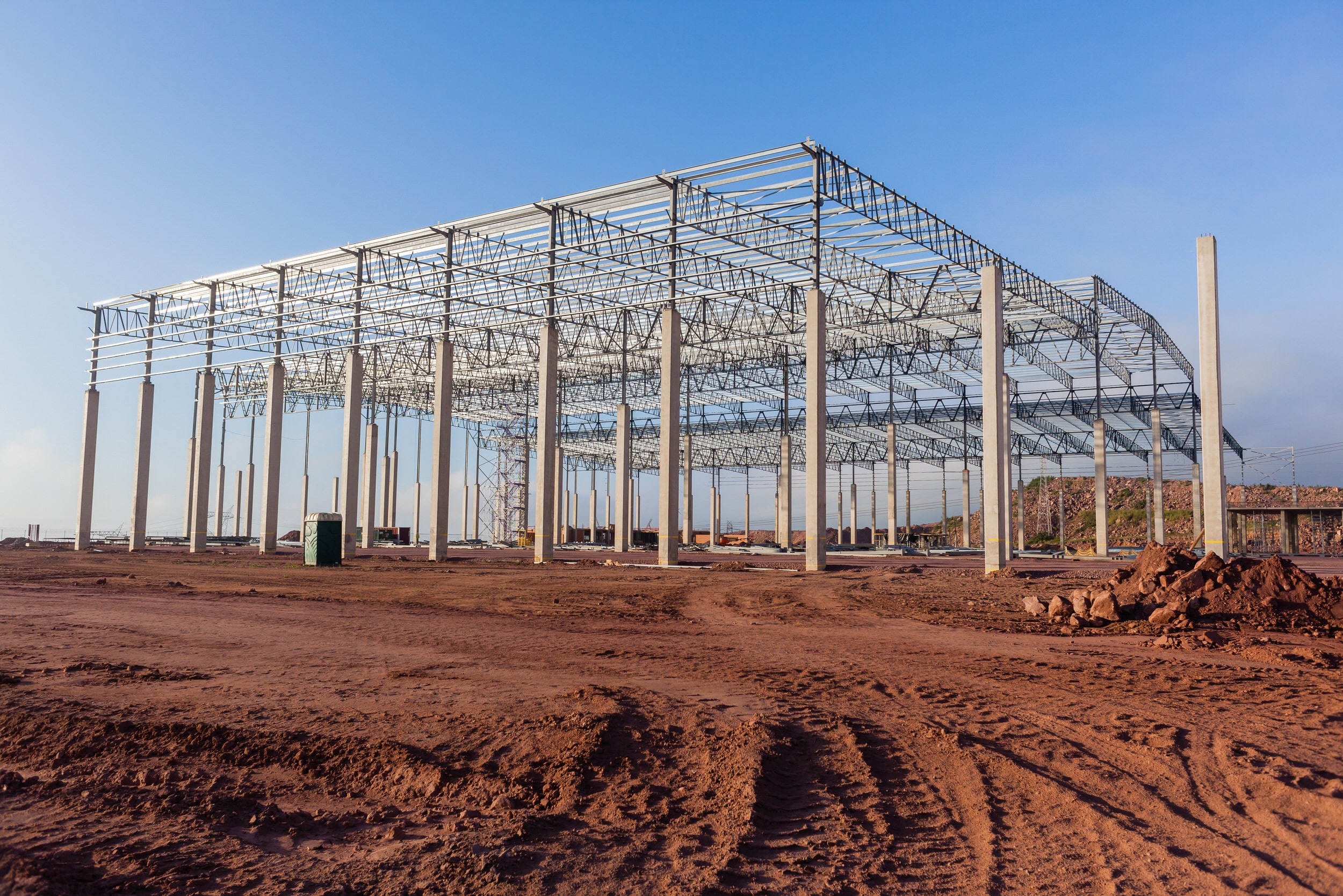 Building new large warehouse construction halfway concrete columns steel roofing beams structure landscape.